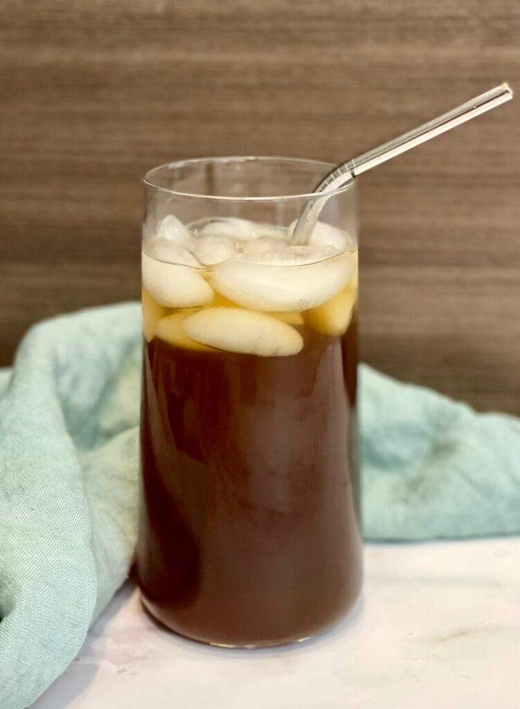 aguapanela served on a clear glass with ice and a metal straw